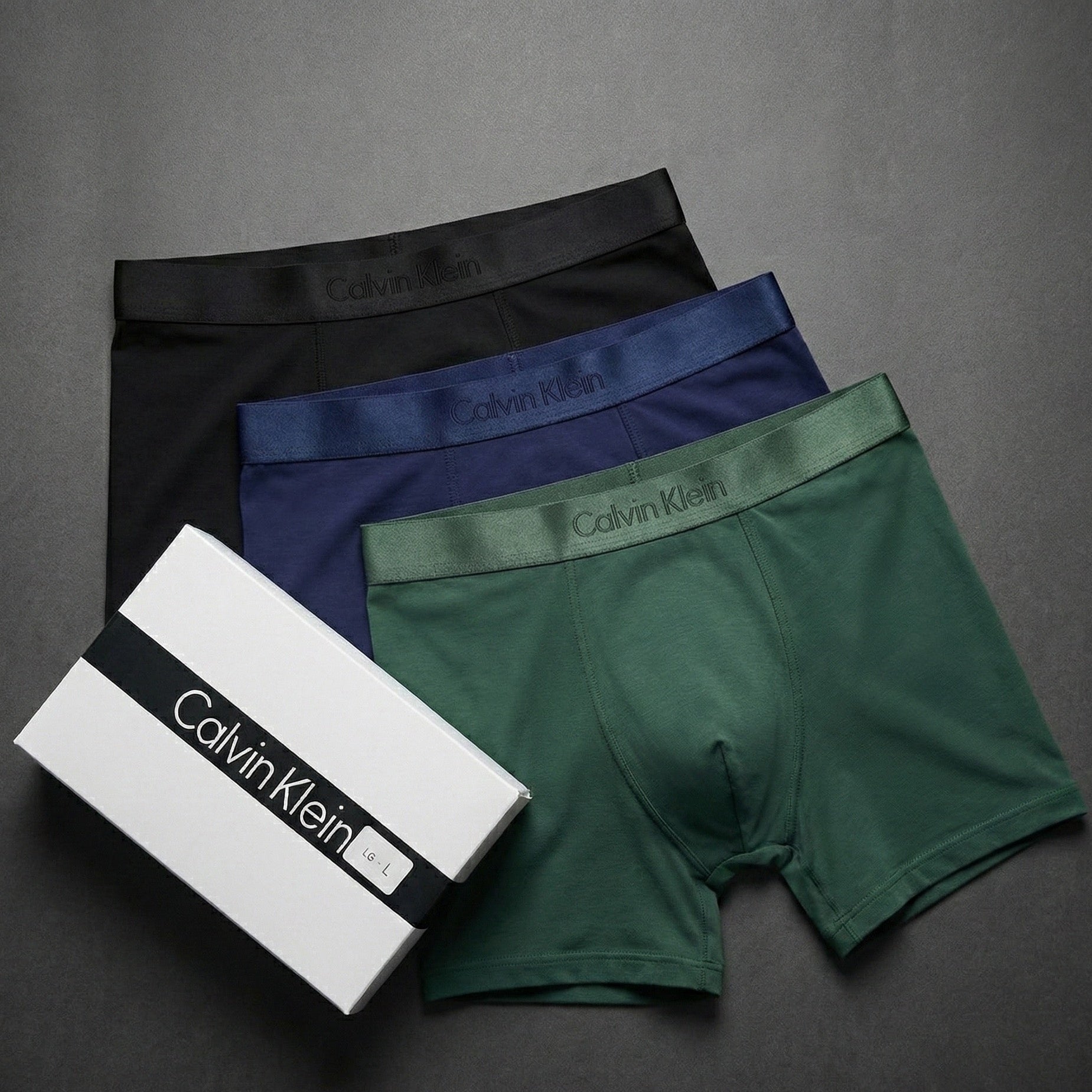 Three pairs of Calvin Klein boxer briefs in black, blue, and green with a white box on a gray background.